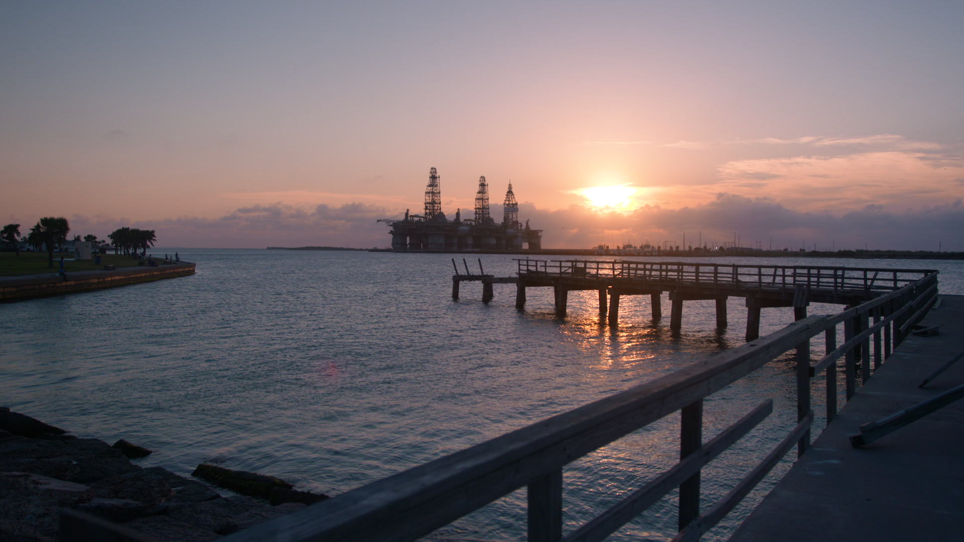The sun sets on a fishing pier, damaged by Hurricane Harvey in 2017, in Port Aransas, Texas. Three offshore oil rigs stand at attention in the distance. (Kevin Clancy / Newsy)